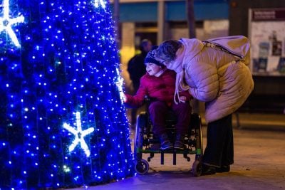 Happy child with disability admiring christmas tree lights with mother at night
