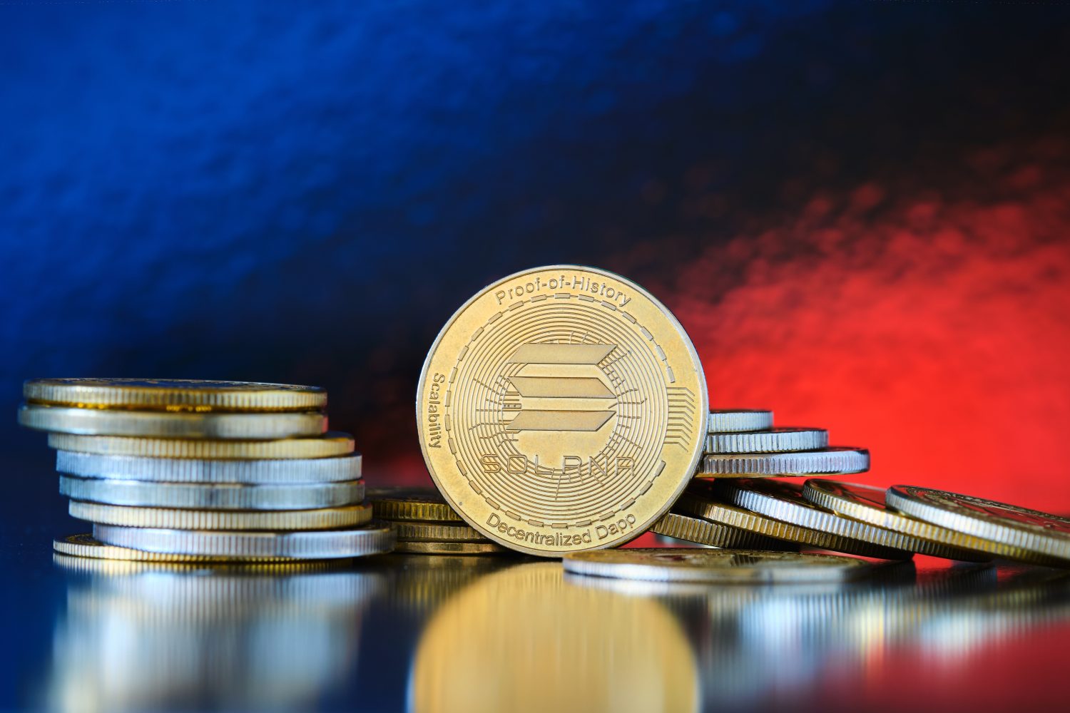 A collection of shiny Solana coins sits on a reflective surface, illuminated by a vibrant red and blue background, highlighting the value and appeal of the cryptocurrency.