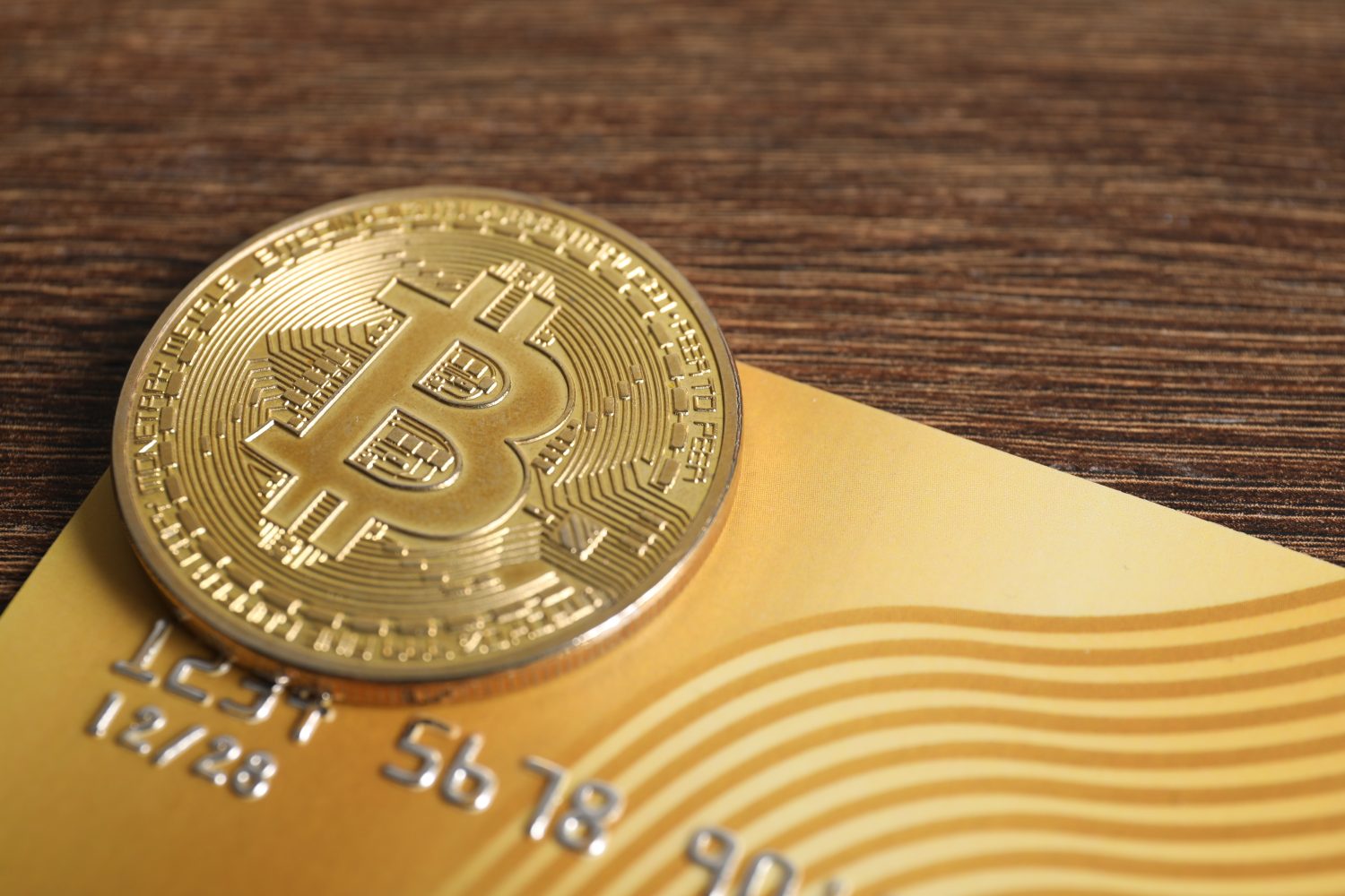 Bitcoin and plastic bank card on wooden table, closeup