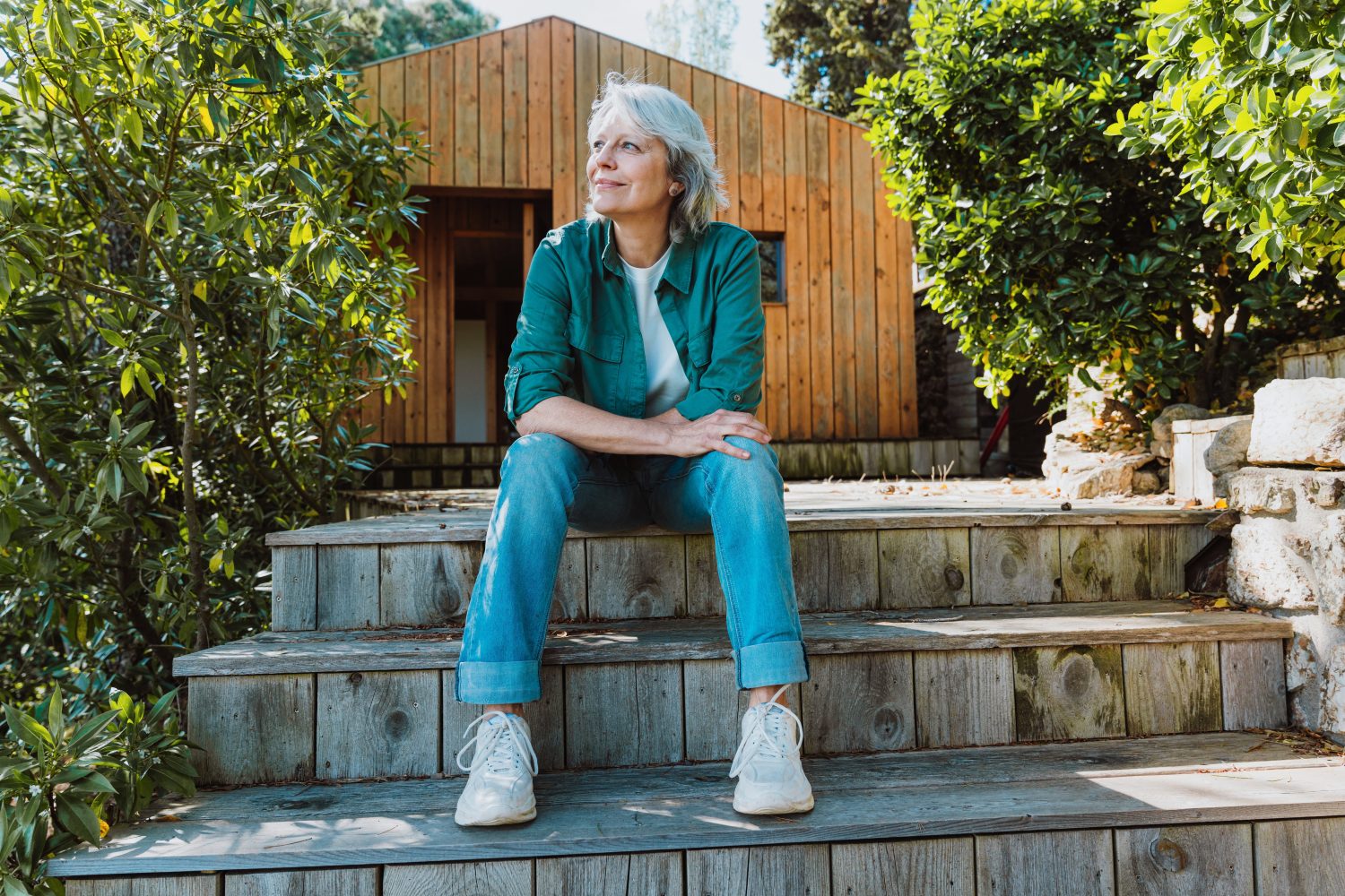 Senior woman relaxing on rustic wooden stairs, looking thoughtfully into the distance, embracing a peaceful outdoors