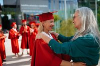 Grandmother hugging granddaughter after successful graduation ceremony outdoors.
