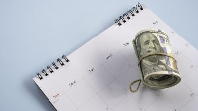 Roll of US dollar bills sitting on top of a monthly desk calendar planner concept of financial deadlines tax day payment schedule or savings