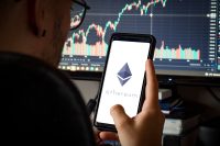 Man with glasses holding phone with crypto asset Ethereum on screen and defocused chart background.