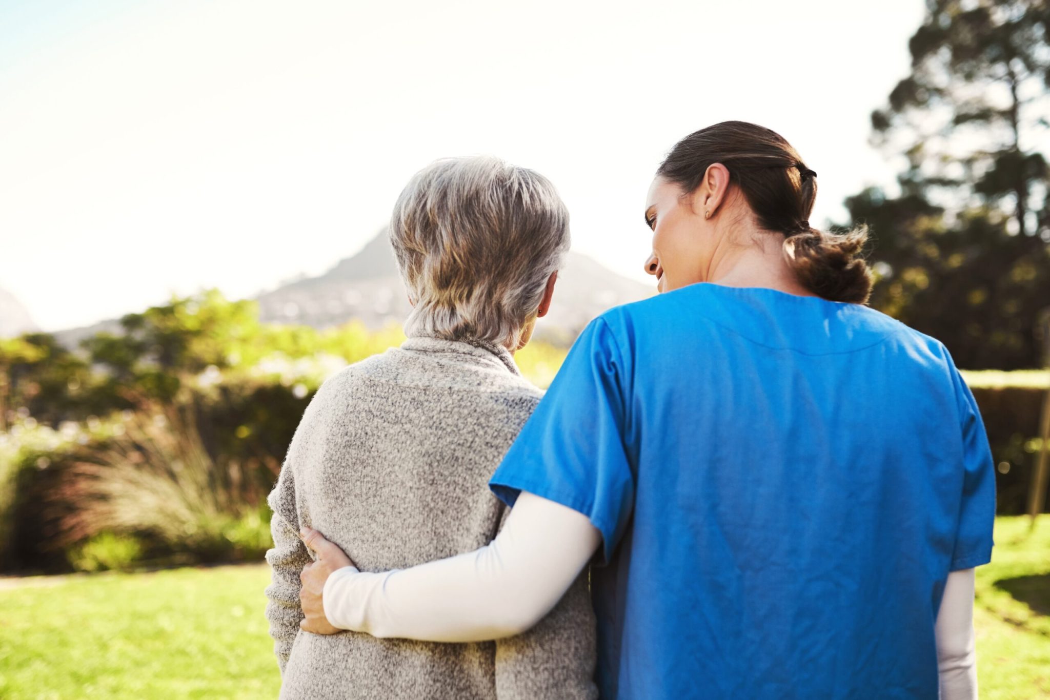 Senior woman, nurse and hug in elderly care, life insurance or support together in nature. Rear view of mature female with caregiver in healthcare, medical aid 