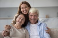 Portrait of young adult caring daughter with mature attractive parents smiling look at camera. Happy multi-generational family enjoy their warm, good, harmonic relationships, showing unity and support