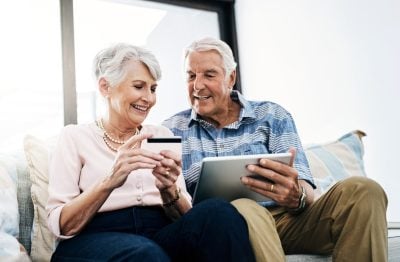 Senior couple, home and tablet with credit card on sofa for online shopping, payment and retirement plan. People, happy and couch at living room for internet banking, budget and investment or finance