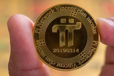 Cryptocurrency concept. two male fingers holding a shiny Pi Network cryptocurrency coin in front of a blurred background. selective focus