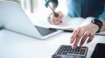 Close up business woman working, using calculator to calculate home finance, accounting with laptop computer on office table, budget management. Doing finance, budgeting and tax calculation.