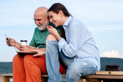Old grandad and young grandchild using laptop. Young girl and old father using laptop, surfing internet outdoor. Younger generation. Caring about older relatives. Old young with laptop concept.