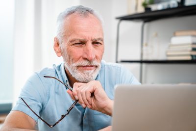 Happy smiling mature Caucasian business man ceo trader using computer, typing, working in modern office, doing online data market analysis, thinking planning tech strategy looking at laptop.