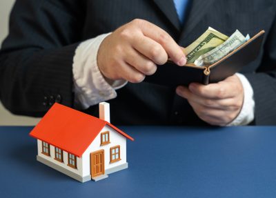 A businessman counts money near a suburban house. Household bills and maintenance. Monthly mortgage payments. family budgeting, rising living costs, finance planning for real estate.