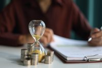Coin stacks and sand clock on the table. Growing of income, saving or return investment through time. Time and money concept.