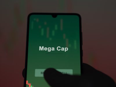An investor analyzing the mega cap etf fund on a screen. A phone shows the prices of Mega Cap