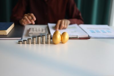 Rising stack of coins and golden eggs on the table. Businessman calculating dividend yield on the background for wealth management and investment concept.