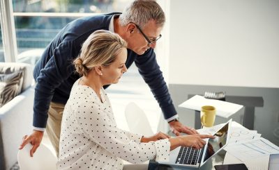Mature couple, laptop and talking with point for financial planning, investment or budget for retirement. Man, woman and tech with paperwork for online banking, account or tax savings in home