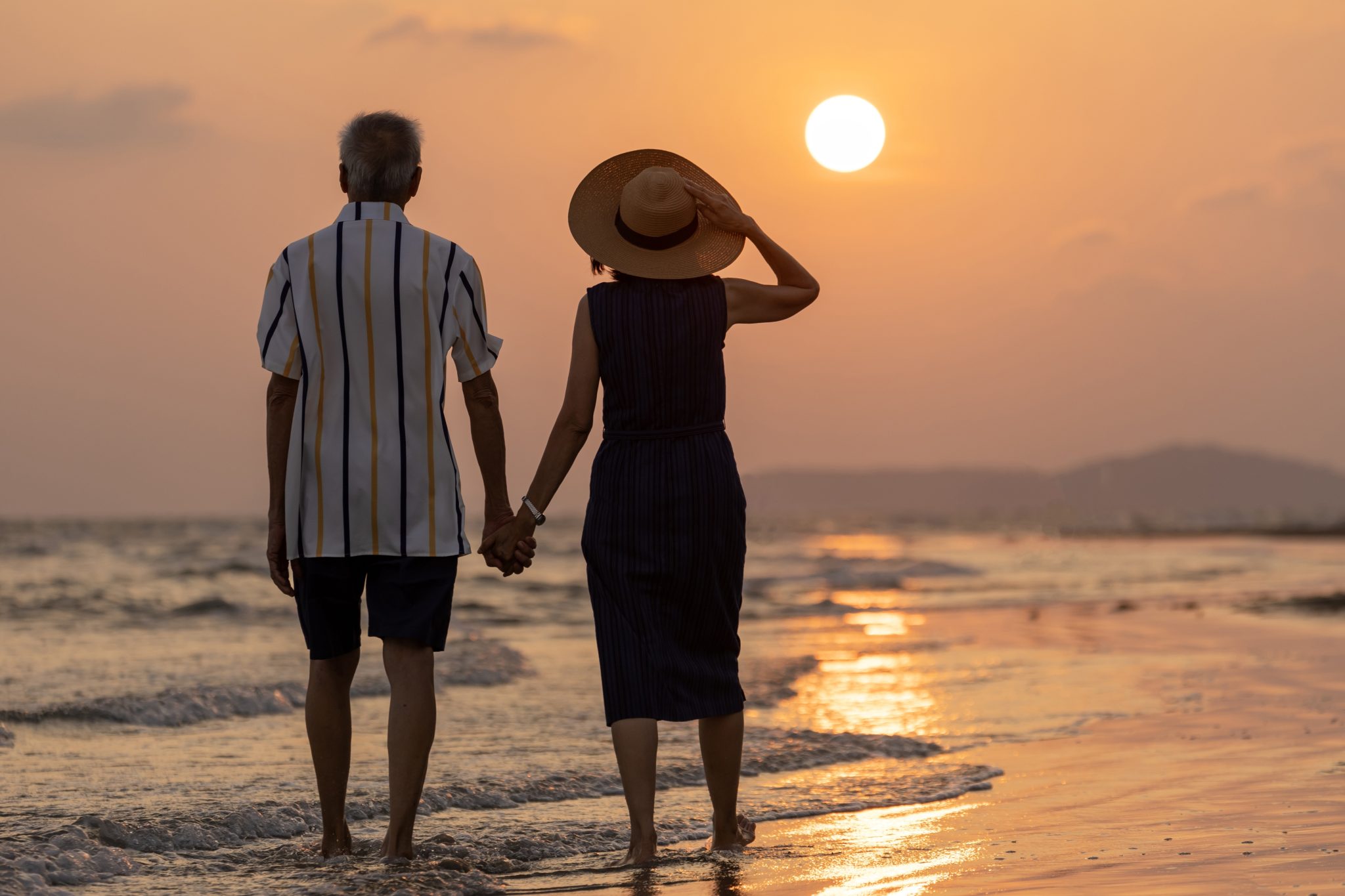 Silhouette of Asian senior couple enjoying their vacation at the sunset sea beach in summer for healthy relationship and happy loving marriage life in retireme