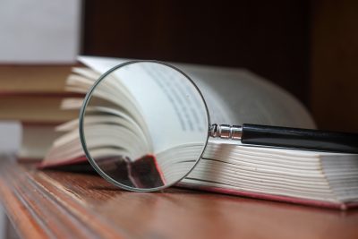 Book and magnifying glass on wooden desk. Searching for Knowledge with Books Concept.