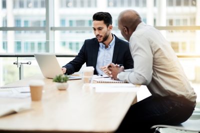 Business, men and meeting with laptop in office for market analysis, investment advice or planning. Stock broker, client and tech with discussion for portfolio management, financial news and feedback